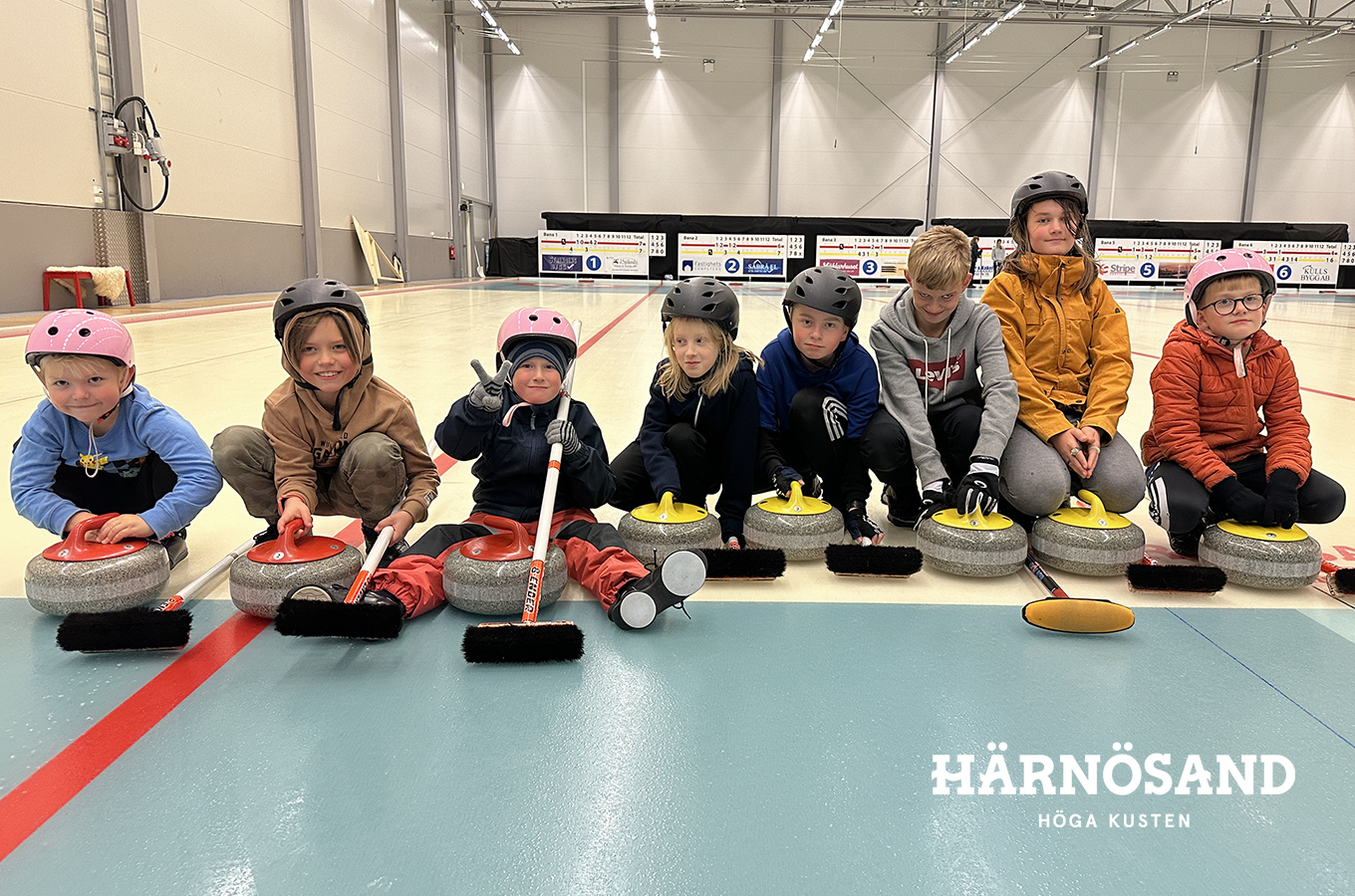 sju barn sitter på rad på is med varsin curlingsten