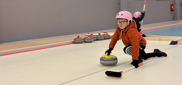 ett barn med hjälm spelar en curlingsten