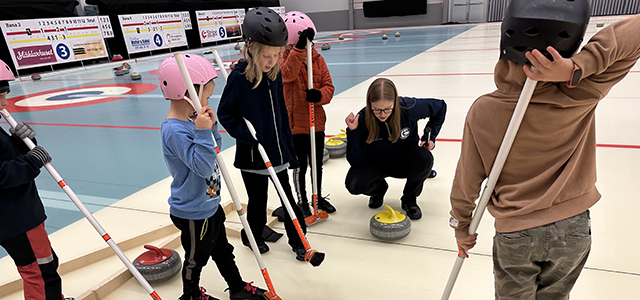 en ungdomsledare står vid en curlingsten och pratar med flera barn